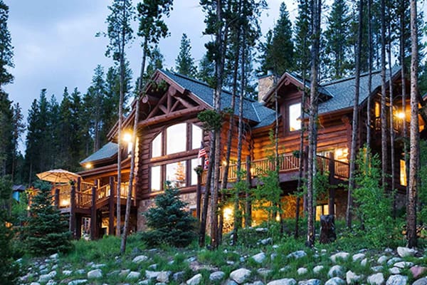 Large three story log home nestled in the hillside with trees surrounding it.
