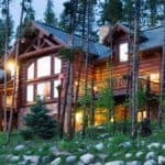 Three story Scandinavian Full-Scribe log home at twilight with exterior lights on. House sits into a wooded hillside.