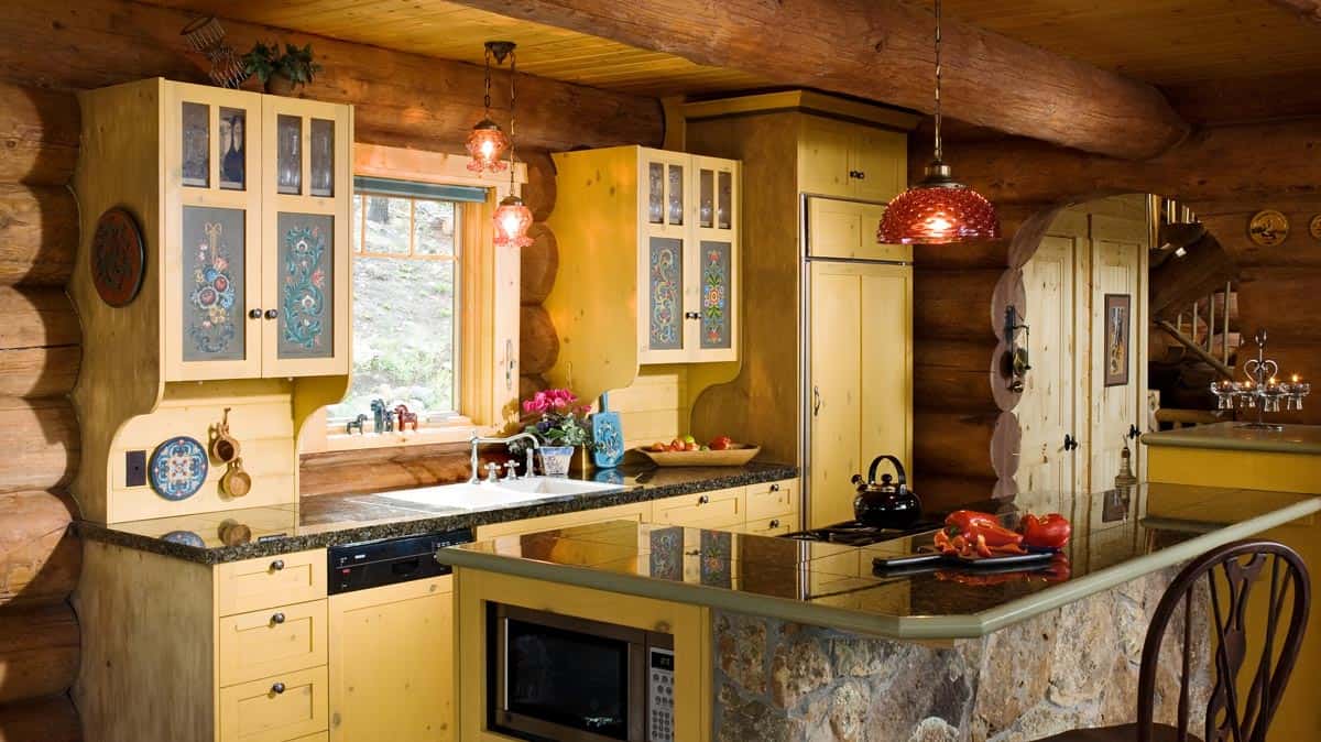 Kitchen in a log hoje with rustic yellow cabinets and L-shaped island.