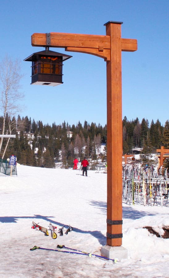 Custom wood built light post at a ski resort with a gas lantern hanging from it. Skis and snow surrounding it.