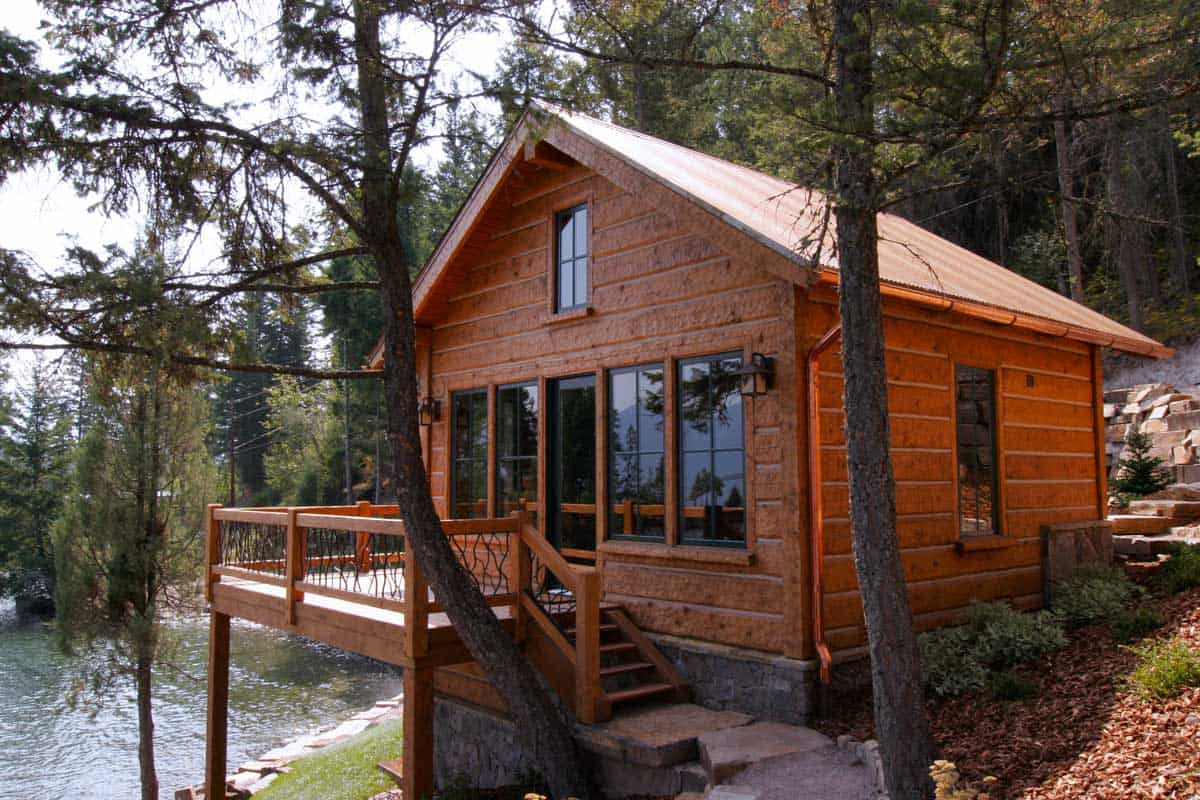 Small log cabin with a deck overlooking a lake.