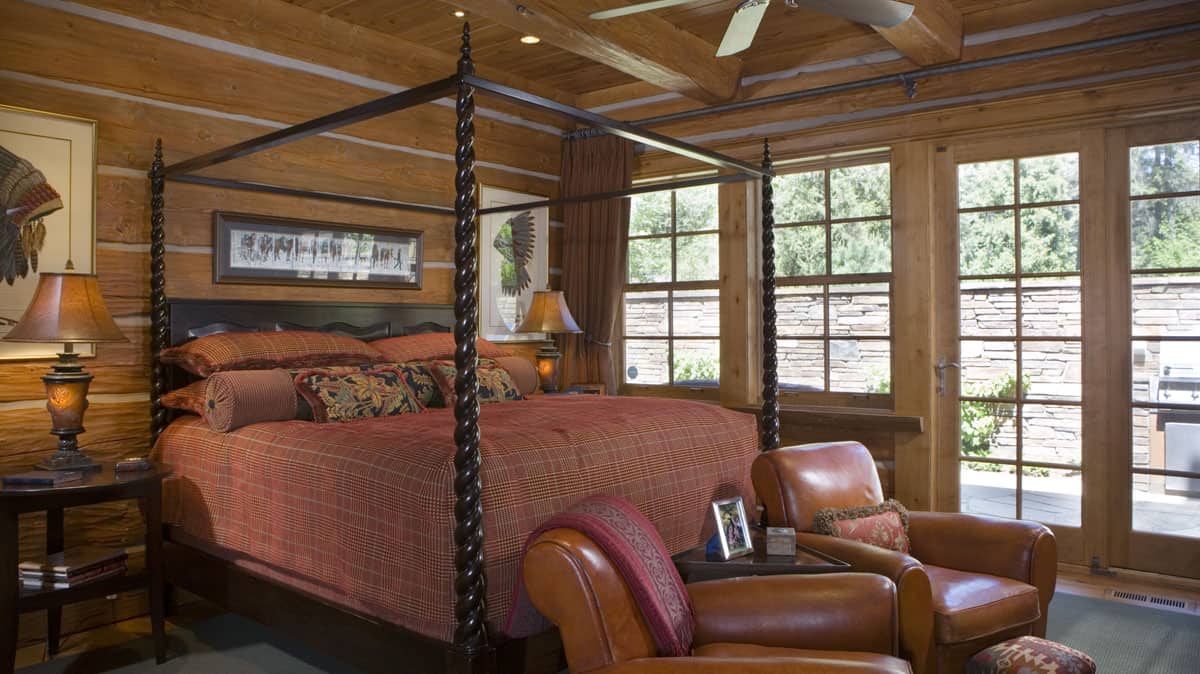 bedroom with a canopy bed, two leather chairs and floor to ceiling pane windows.