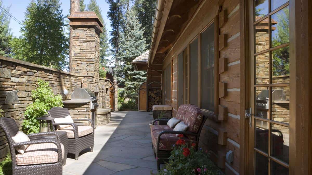 Outside seating area nestled between a high rock wall, with large outdoor fireplace, and an Appalachian Dovetail Log home.