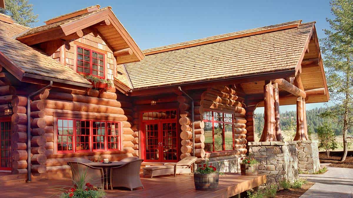 Deck and log home built in a Scandinavian Full-Scribe style with red window panes.