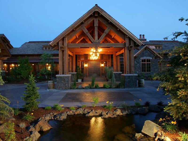Picture of a golf club portico built with timber frame and a large chandelier illuminated at dusk. A pond is in the foreground with the driveway between the pond and the entry way.