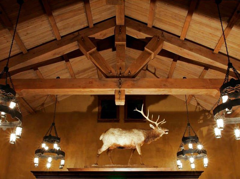 Picture of a ceiling that's been custom built with wood timber, four metal chandeliers are hanging from it and a mounted caribou sits up high on a shelf.