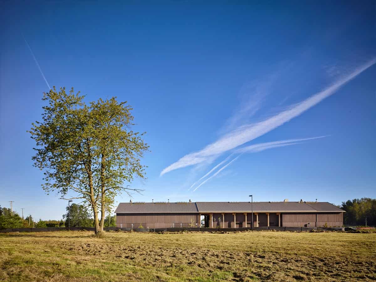 Large commercial smokehouse with fields around it and a large tree with blue sky.