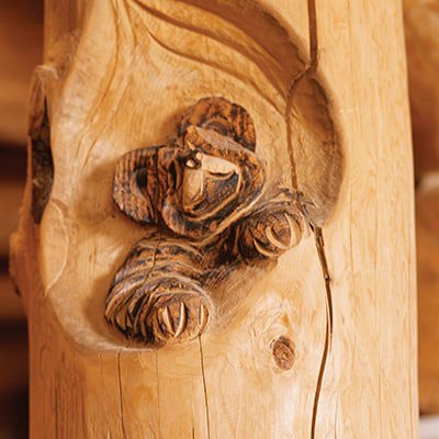 Face, ears and front paws of a bear cub carved out of wood on a interior house support beam.
