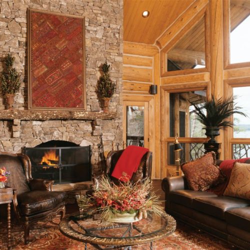 Custom log home living room with warm fireplace, decorated with splashes of red.