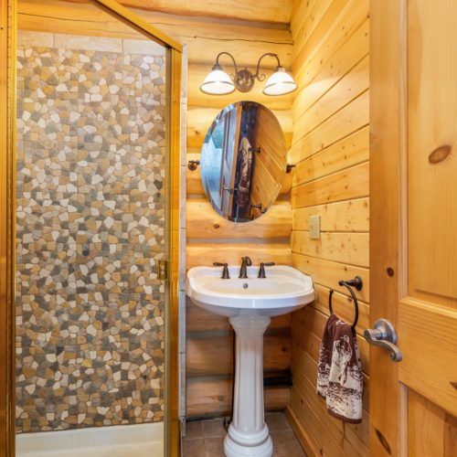 Adorable pedestal sink and custom stone shower give this cute log cabin bathroom a touch of modern.